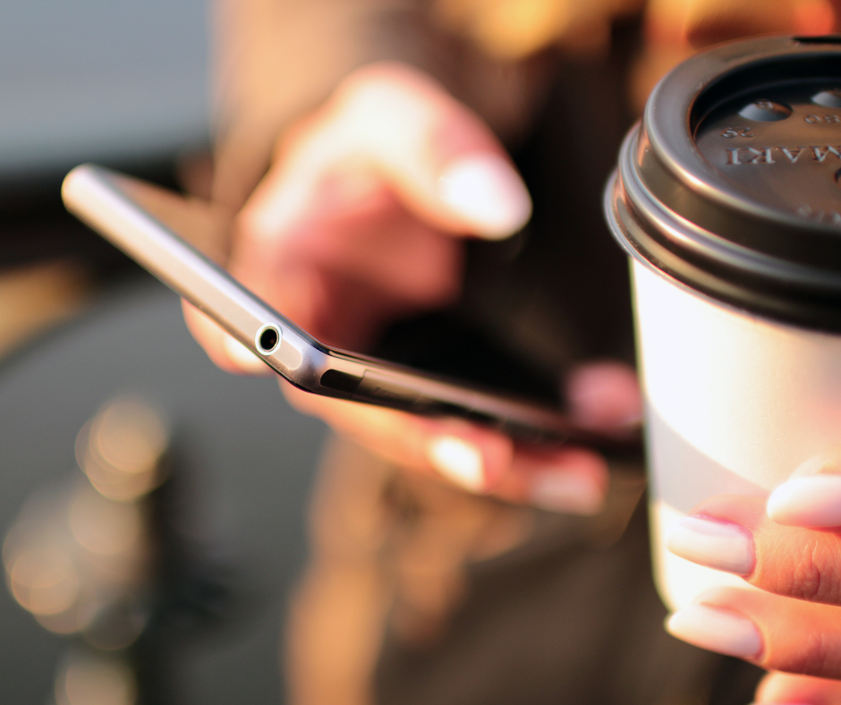 a person holding a phone in one hand and a coffee in the other.